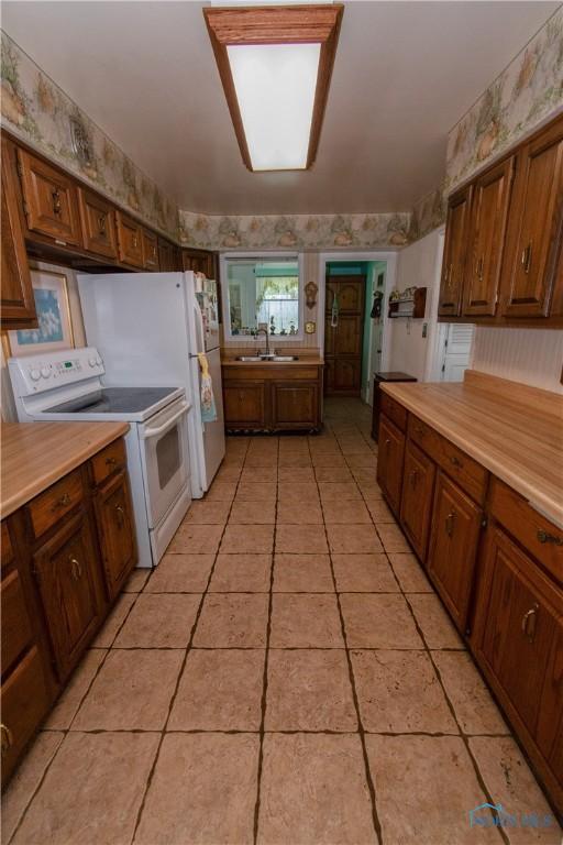 2823 Wicklow Rd, Toledo, OH 43606 - kitchen with electric range, wallpapered walls, light countertops, light tile patterned flooring, and brown cabinets
