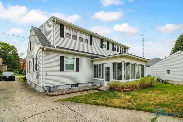 1013 Whittlesey St, Fremont, OH 43420 - view of front facade with a sunroom, a front lawn, and driveway