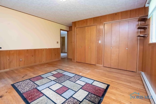 1527 Lockwood Rd, Findlay, OH 45840 - unfurnished bedroom with a baseboard radiator, multiple closets, wood finished floors, wooden walls, and wainscoting