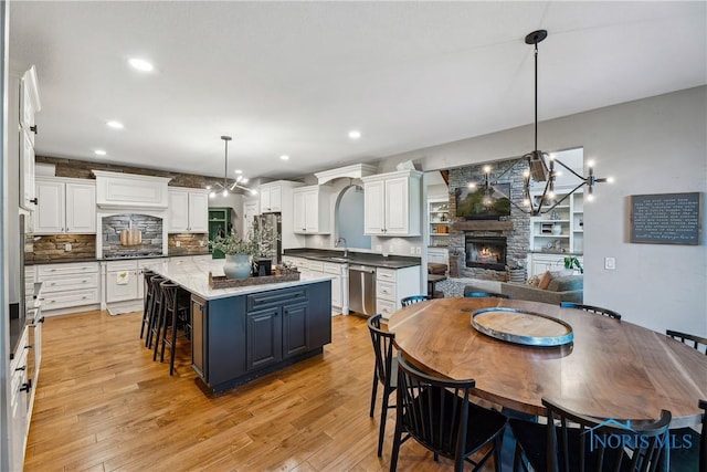 4811 Yosemite Pkwy, Sylvania, OH 43560 - kitchen with appliances with stainless steel finishes, a stone fireplace, white cabinets, a breakfast bar, and light wood finished floors