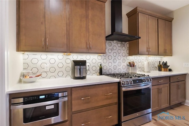 1635 Winterwood Ct, Bowling Green, OH 43402 - kitchen featuring wall chimney exhaust hood, stainless steel appliances, light countertops, decorative backsplash, and light wood-type flooring