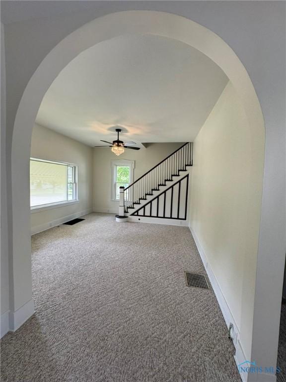 201 E Rings St, West Unity, OH 43570 - carpeted empty room with stairs, a ceiling fan, and arched walkways