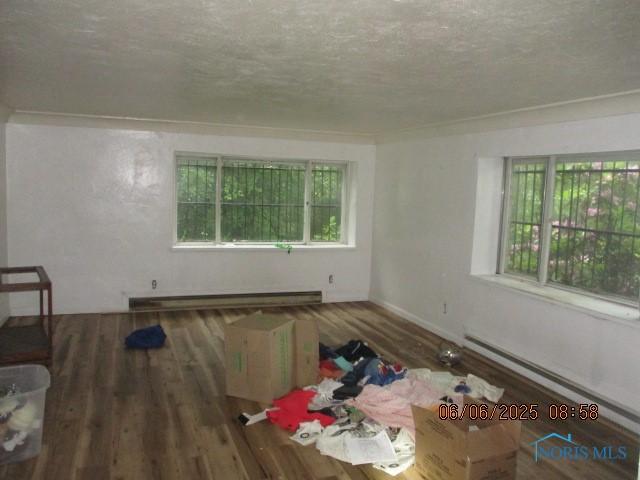100 S Crissey Rd, Holland, OH 43528 - unfurnished living room featuring baseboard heating, a textured ceiling, wood finished floors, and a baseboard heating unit
