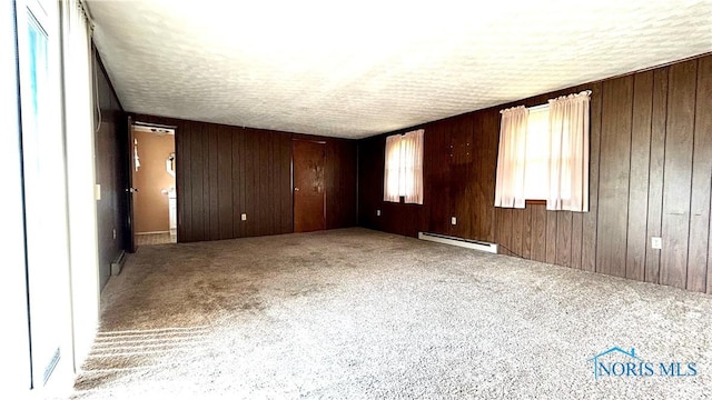 825 Johnson Rd, Paulding, OH 45879 - carpeted empty room featuring baseboard heating, a textured ceiling, and wooden walls