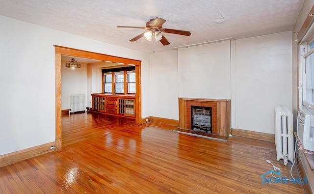 433 Islington St, Toledo, OH 43610 - unfurnished living room with radiator heating unit, a ceiling fan, a brick fireplace, wood-type flooring, and a textured ceiling
