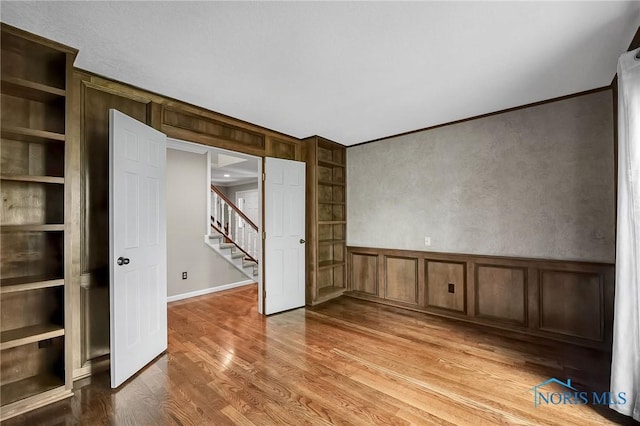 1626 Woodstream Rd, Perrysburg, OH 43551 - unfurnished room with stairway, light wood-style floors, a decorative wall, built in shelves, and crown molding