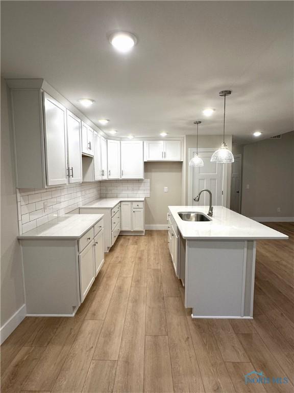 7811 Sonoma Dr, Monclova, OH 43542 - kitchen featuring light wood finished floors, tasteful backsplash, white cabinets, a kitchen island with sink, and decorative light fixtures