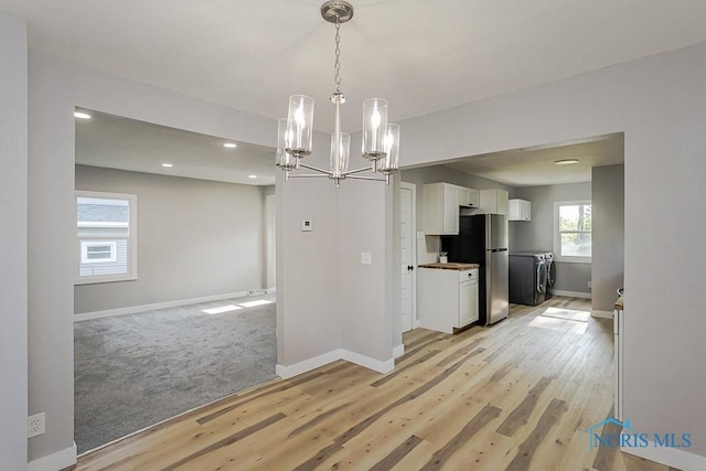 2242 Vaness Dr, Toledo, OH 43615 - kitchen featuring freestanding refrigerator, white cabinetry, washing machine and clothes dryer, a chandelier, and light wood finished floors