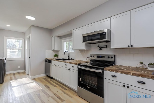 2242 Vaness Dr, Toledo, OH 43615 - kitchen with appliances with stainless steel finishes, butcher block counters, light wood-style flooring, decorative backsplash, and white cabinets