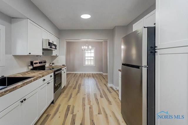 2242 Vaness Dr, Toledo, OH 43615 - kitchen featuring appliances with stainless steel finishes, white cabinetry, a chandelier, light wood-style flooring, and decorative light fixtures