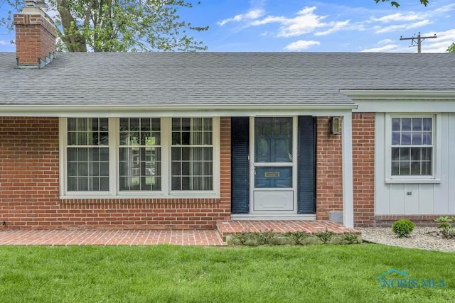3733 Shamrock Dr, Toledo, OH 43615 - view of exterior entry featuring a chimney, a lawn, brick siding, and a shingled roof