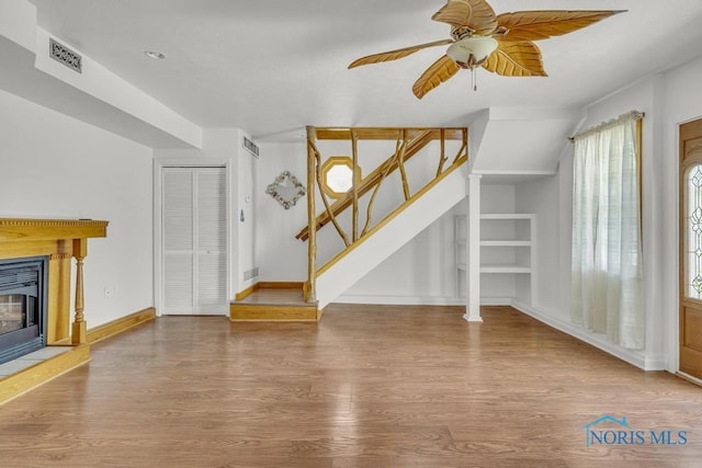 3133 126th St, Toledo, OH 43611 - unfurnished living room with wood finished floors, ceiling fan, stairs, built in shelves, and a glass covered fireplace