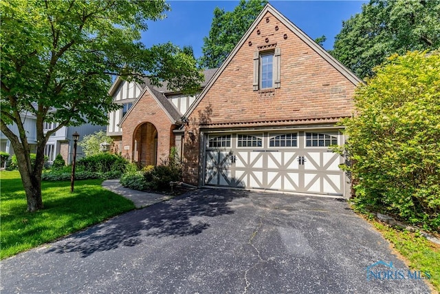 2325 Saint Roberts Ln, Toledo, OH 43617 - tudor-style house with an attached garage, driveway, a front yard, and brick siding