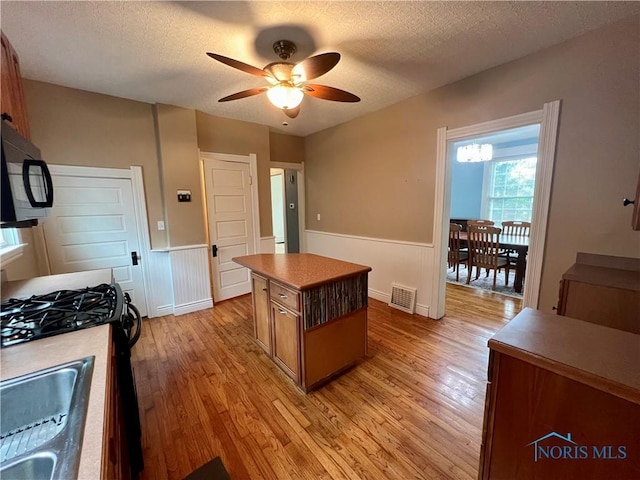 1810 E Broadway St, Toledo, OH 43605 - kitchen with black microwave, light wood-type flooring, a ceiling fan, wainscoting, and range with gas cooktop