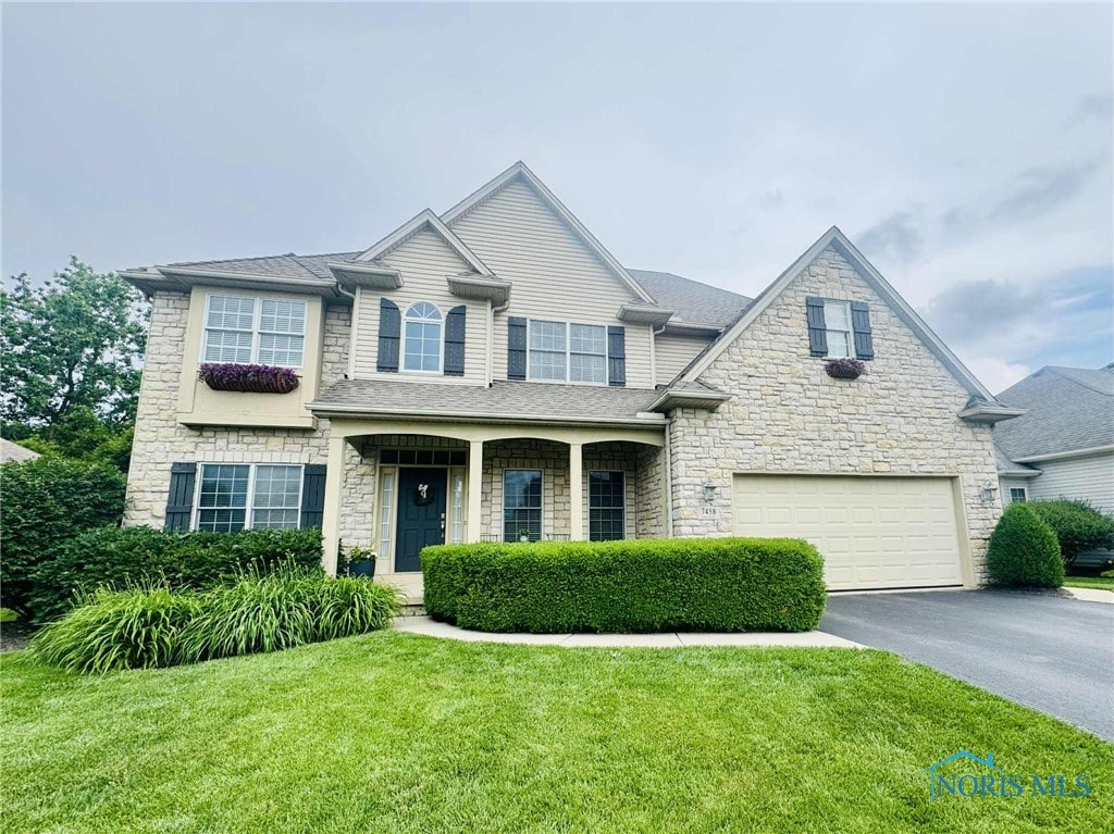7458 Kaolin Rd, Maumee, OH 43537 - view of front facade featuring a garage, asphalt driveway, stone siding, and a front yard