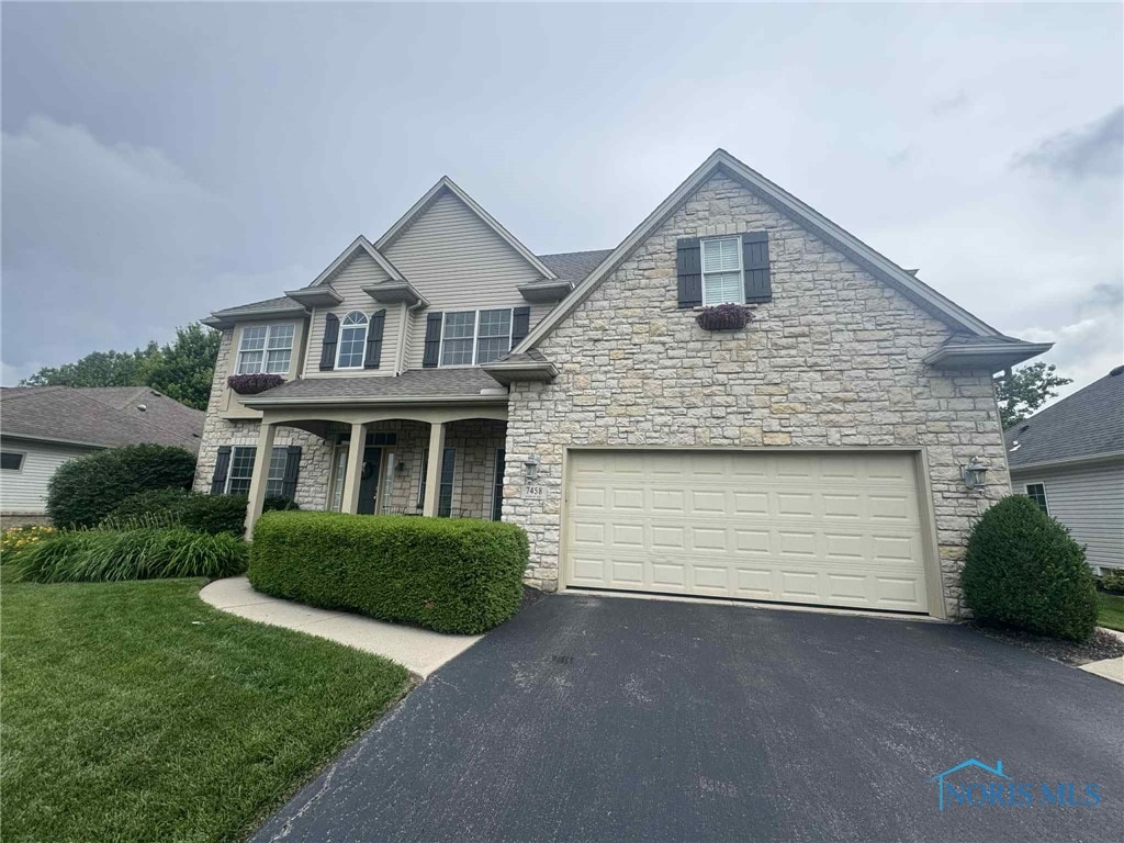 7458 Kaolin Rd, Maumee, OH 43537 - view of front of house with stone siding, asphalt driveway, an attached garage, and a front yard