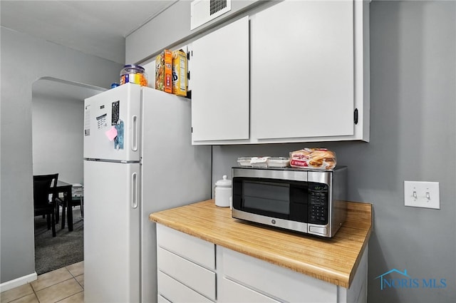 1732 Gilbert Rd, Toledo, OH 43614 - kitchen featuring stainless steel microwave, white cabinets, freestanding refrigerator, light tile patterned floors, and light countertops
