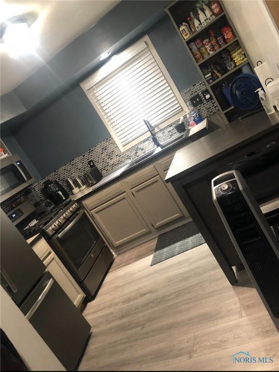 1708 Fredonia Ave, Toledo, OH 43608 - kitchen with stainless steel microwave, light wood-type flooring, dark countertops, and tasteful backsplash