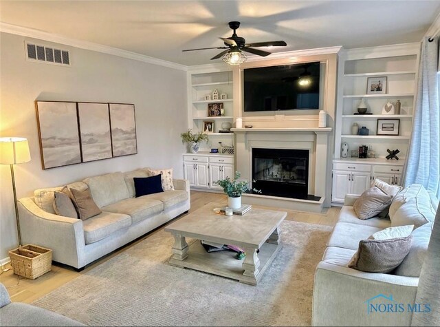 2456 Wembley Ter, Toledo, OH 43617 - living area with a ceiling fan, ornamental molding, a glass covered fireplace, built in shelves, and light wood finished floors