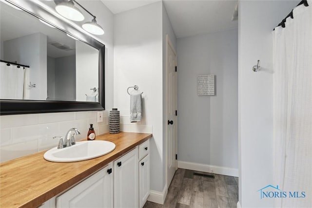 735 Hemlock St, Wauseon, OH 43567 - full bathroom featuring wood finished floors, vanity, decorative backsplash, and curtained shower