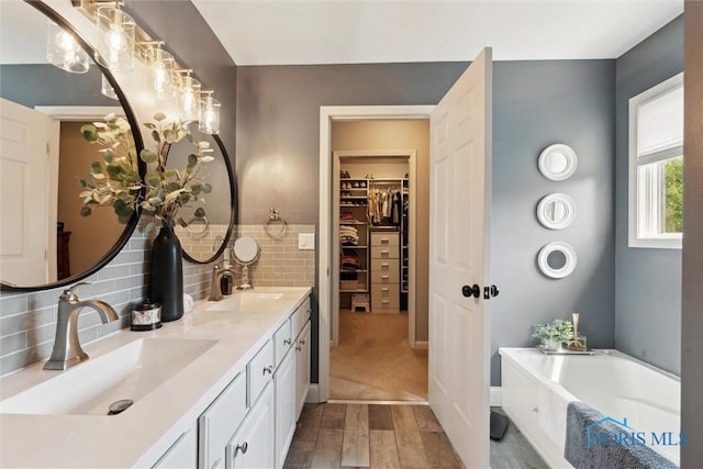 735 Hemlock St, Wauseon, OH 43567 - full bathroom with double vanity, a garden tub, wood finished floors, a spacious closet, and decorative backsplash