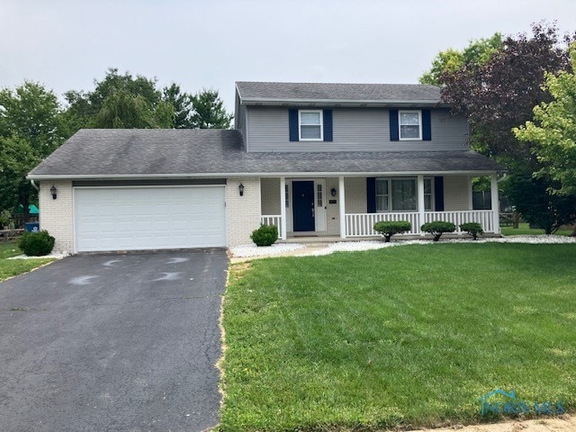 491 Patriot Dr, Waterville, OH 43566 - view of front of home with covered porch, driveway, an attached garage, a front lawn, and brick siding
