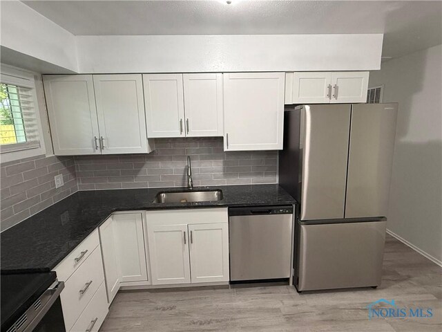 3209 Romaker Rd, Toledo, OH 43615 - kitchen with appliances with stainless steel finishes, backsplash, dark stone counters, light wood-style flooring, and white cabinetry