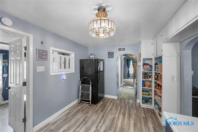 411 Seneca St, Defiance, OH 43512 - kitchen featuring arched walkways, freestanding refrigerator, light wood finished floors, white cabinets, and a chandelier