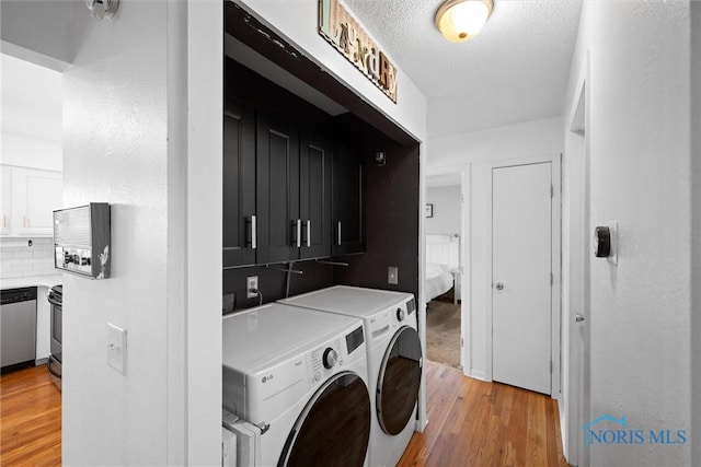 3005 Springwood St, Oregon, OH 43616 - laundry area featuring separate washer and dryer, light wood-style flooring, a textured ceiling, and cabinet space