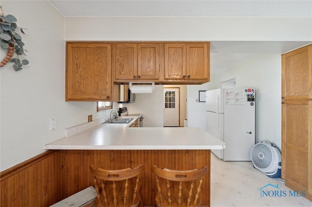 17918 Dunbridge Rd, Bowling Green, OH 43402 - kitchen with white appliances, a peninsula, light countertops, brown cabinetry, and a kitchen breakfast bar