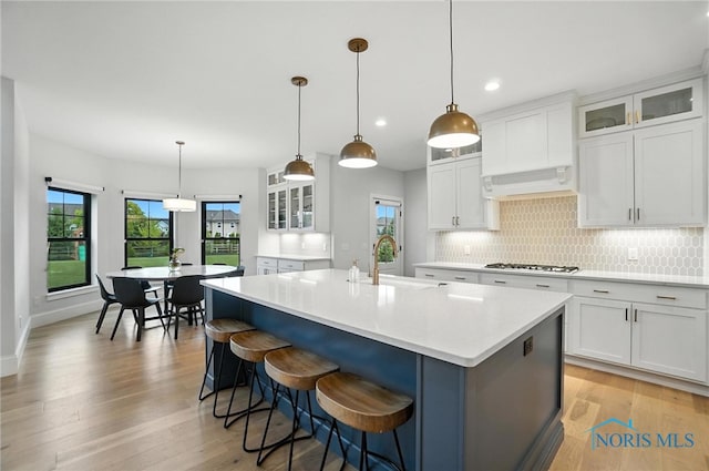 4214 Thornbury Ct, Perrysburg, OH 43551 - kitchen featuring gas stovetop, premium range hood, a center island with sink, tasteful backsplash, and light wood-type flooring