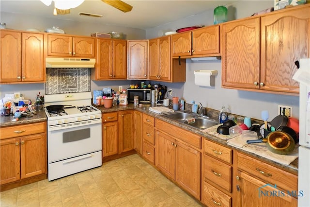 912 Virginia St, Port Clinton, OH 43452 - kitchen featuring white gas range oven, under cabinet range hood, stainless steel microwave, ceiling fan, and brown cabinetry