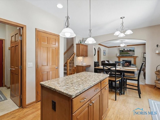 646 Whisperlake Rd, Holland, OH 43528 - kitchen featuring arched walkways, light wood-style flooring, a lit fireplace, a kitchen island, and hanging light fixtures