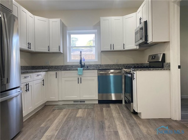 5240 Rambo Ln, Toledo, OH 43623 - kitchen featuring appliances with stainless steel finishes, dark stone counters, wood finished floors, and white cabinets
