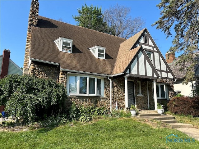 1619 Addington Rd, Toledo, OH 43607 - tudor-style house with stone siding, a chimney, a front lawn, and roof with shingles