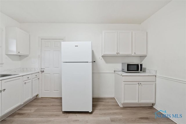 3042 Schneider Rd, Toledo, OH 43614 - kitchen featuring freestanding refrigerator, stainless steel microwave, white cabinetry, and light wood-style flooring