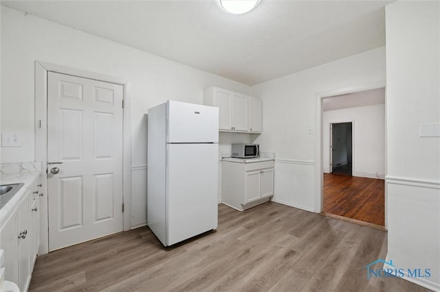 3042 Schneider Rd, Toledo, OH 43614 - kitchen featuring freestanding refrigerator, stainless steel microwave, light wood-type flooring, and white cabinetry