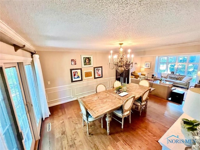 2720 Derby Rd, Ottawa Hills, OH 43615 - dining space featuring a textured ceiling, a chandelier, crown molding, wood finished floors, and a wainscoted wall
