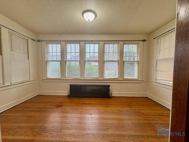 2840 Scottwood Ave, Toledo, OH 43610 - empty room with radiator, plenty of natural light, wood finished floors, and a textured ceiling