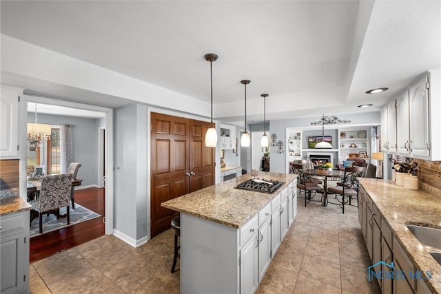 9627 Sheffield Rd, Perrysburg, OH 43551 - kitchen with gas stovetop, white cabinetry, a kitchen island, light stone counters, and a lit fireplace
