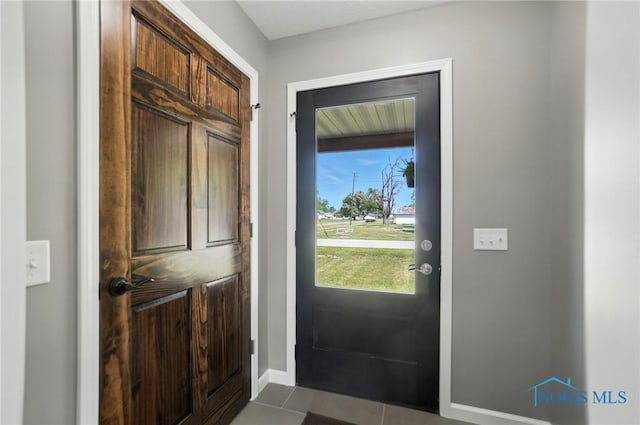 doorway to outside with dark tile patterned flooring and baseboards