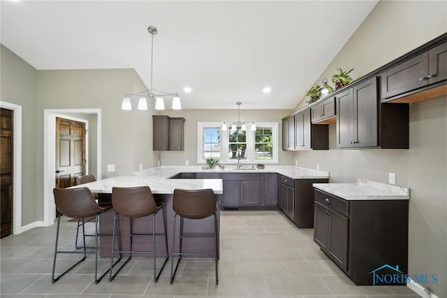 kitchen with a breakfast bar area, dark brown cabinetry, light stone countertops, lofted ceiling, and hanging light fixtures