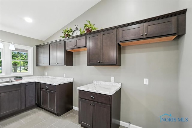 kitchen featuring dark brown cabinetry, vaulted ceiling, light stone countertops, and light tile patterned floors