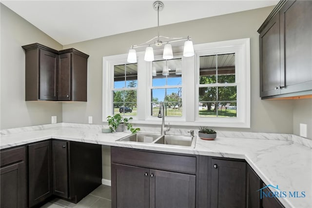 kitchen with dark brown cabinets, light tile patterned floors, light stone counters, and hanging light fixtures