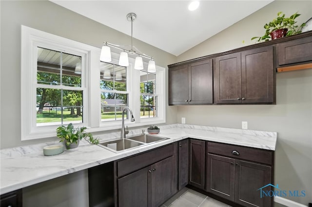 kitchen with dark brown cabinets, lofted ceiling, pendant lighting, light stone countertops, and light tile patterned floors