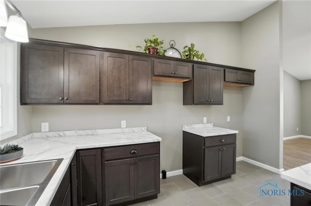 kitchen featuring dark brown cabinetry, light stone counters, light tile patterned flooring, lofted ceiling, and decorative light fixtures