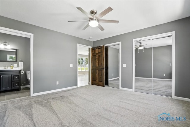 unfurnished bedroom featuring multiple closets, light colored carpet, ensuite bath, and ceiling fan