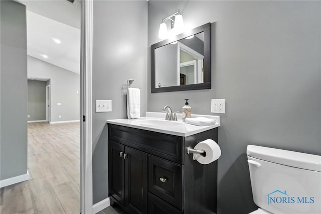 half bath with vanity, wood finished floors, and vaulted ceiling