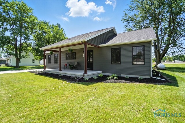 rear view of property with a yard, a porch, and roof with shingles