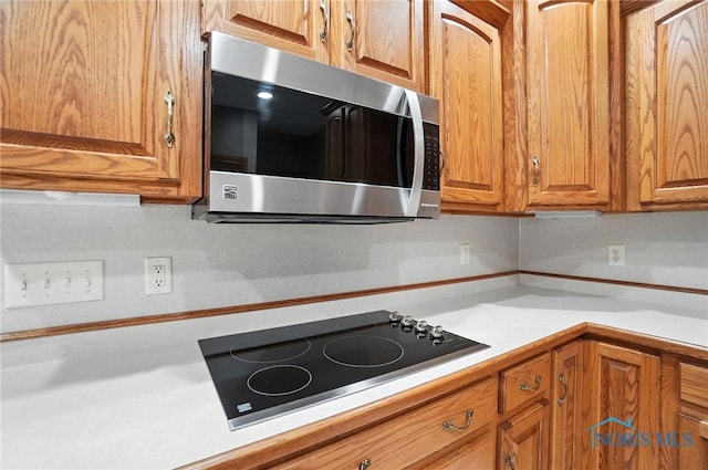 8076 Trent Lock Dr, Waterville, OH 43566 - kitchen with stainless steel microwave, black electric stovetop, light countertops, and brown cabinetry